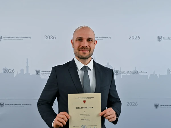 Ein Mann in einem dunklen Anzug hält stolz ein Dokument mit der Beschriftung „BERUFSBILDERUNGE“ und posiert vor einer grafischen Hintergrunddarstellung einer Stadtlandschaft mit dem Jahr 2026.
