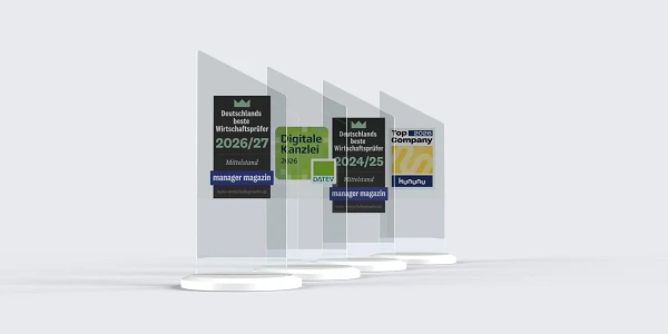 Vier gläserne Auszeichnungen stehen auf weißen Ständern, die mit verschiedenen Titeln und Jahresangaben beschriftet sind, darunter „Deutschlands beste Wirtschaftsspieler 2026/27“, „Digitale Kanzlei 2026“ und „Top ECRS Company“.